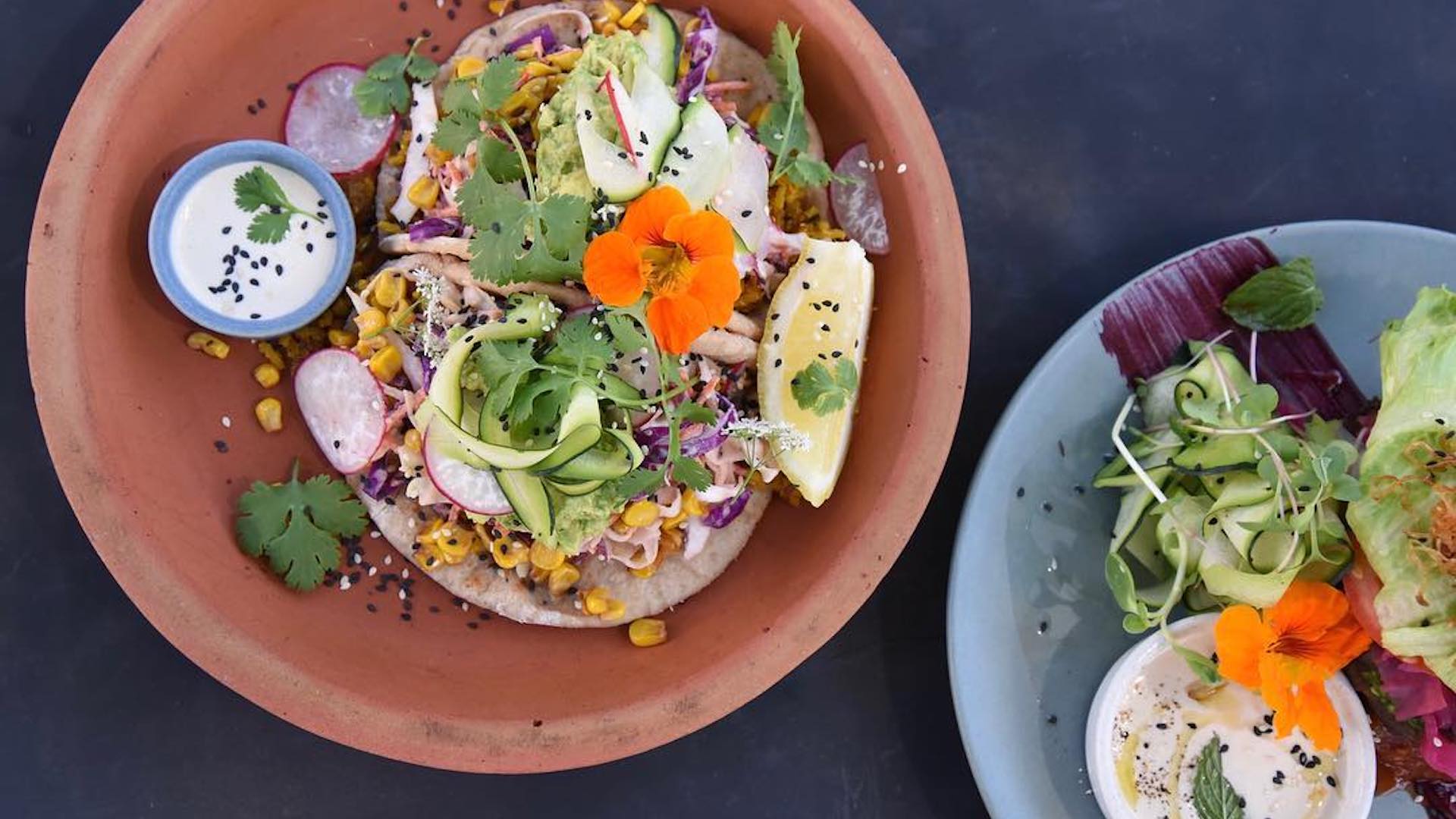 Cafes in QLD with gluten-free menus: Marie Anita's. Image of flatbreads topped with corn, avocado, radishes, coriander, orange edible flowers and served with lemon wedges