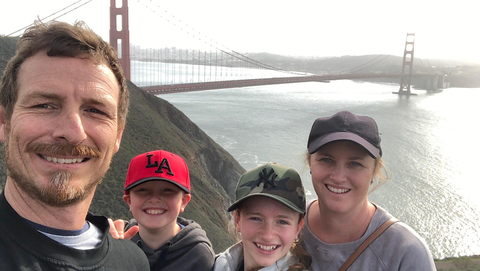 A family with parents and their young son and daughter posing in front of golden gate bridge