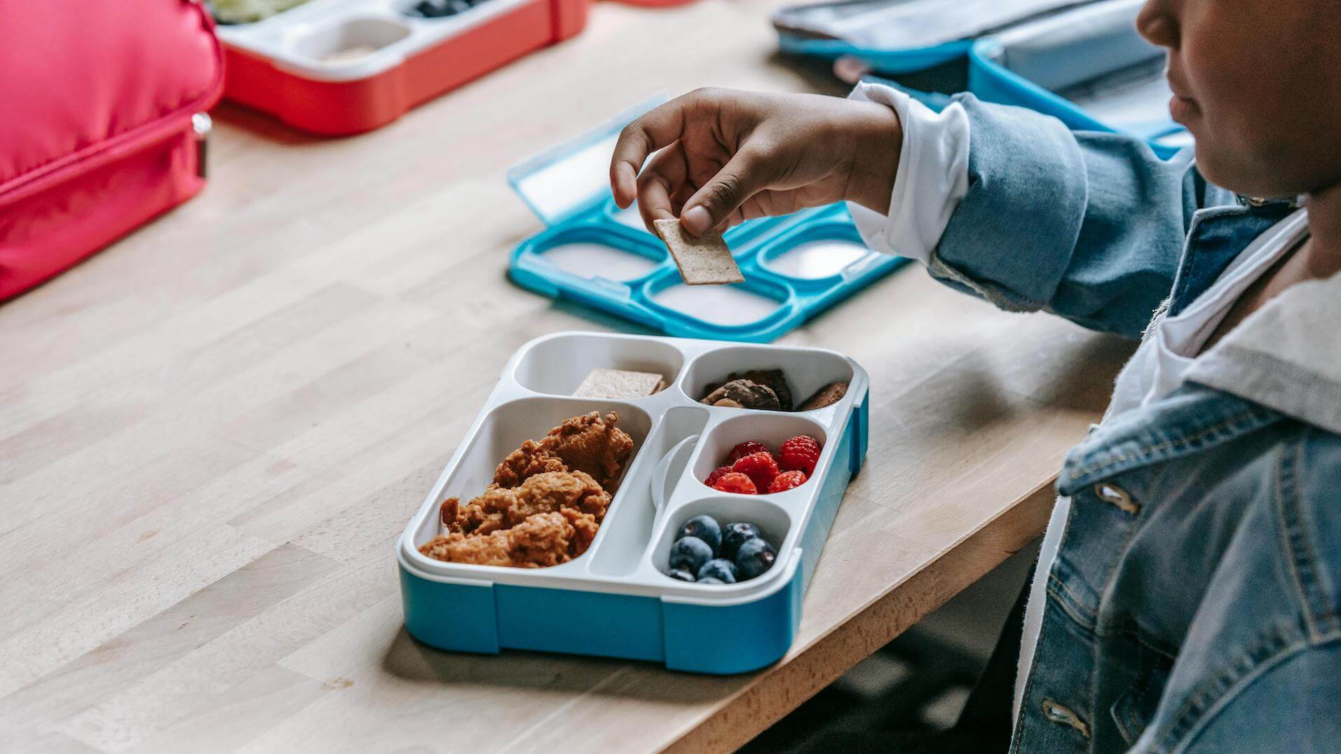 Gluten-free Living: back to school tips and gluten-free lunchbox ideas. Boy at school with his bento-style lunchbox filled with fried chicken, crackers, berries and raspberries.