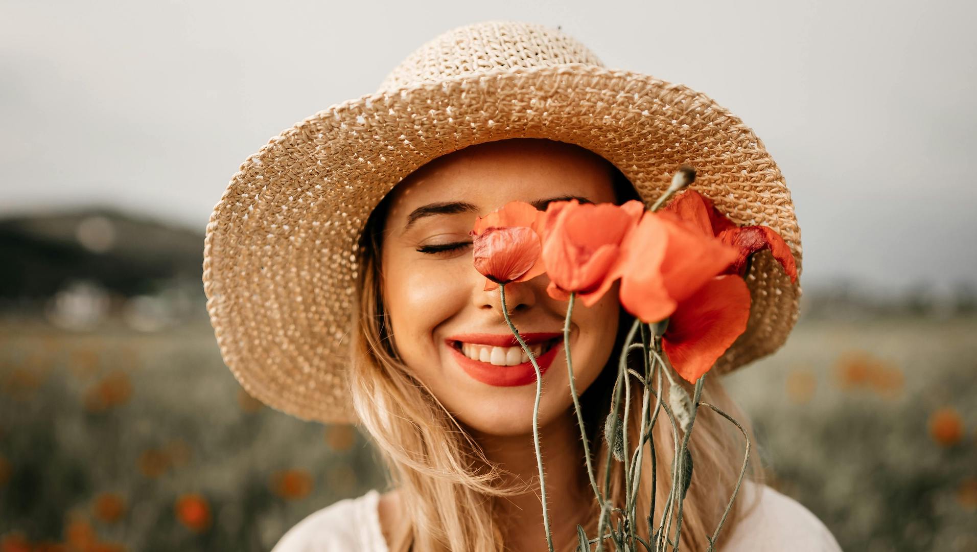 Gluten-Free Living: A young woman in a straw hat standing in a field, holding a bunch of orange tulips to her face, eyes closed and enjoying the moment.