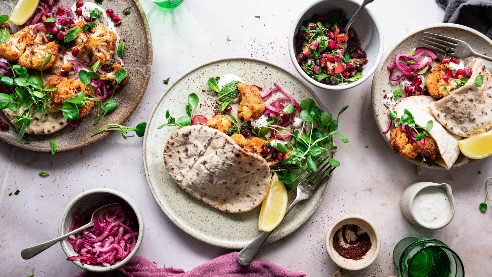 Gluten-free living: a colourful table spread with pita breads filled with spiced cauliflower, with salad, lemon wedges and pomegranate herb salad on the side.